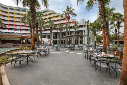 an outdoor patio with tables and chairs and palm trees at Megasaray Resort Side in Side