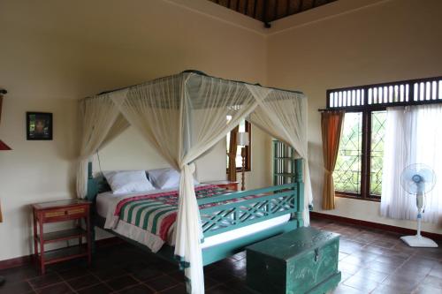 a bedroom with a canopy bed and two windows at Uma Capung Mas Cottage in Ubud