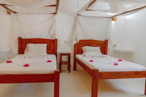 two beds in a room with red flowers on them at Baobab Village in Watamu