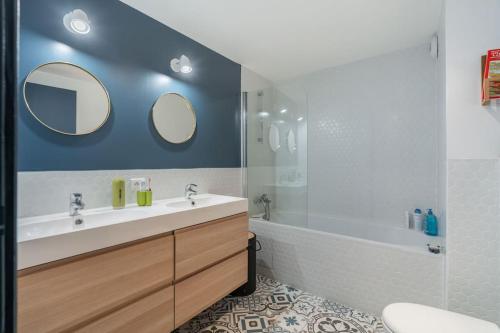 une salle de bain avec un lavabo, une baignoire et deux miroirs dans l'établissement Charmant Appartement Montmartre, à Paris