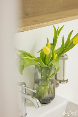 a glass vase with yellow flowers sitting on a sink at Pinea Gold 620 - BASEN, sauna, jacuzzi w cenie pobytu - VI piętro z widokiem na morze in Pobierowo
