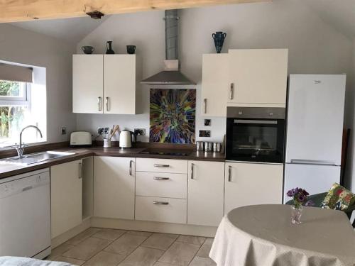 a kitchen with white cabinets and a table in it at Pretty Garden Cottage in Tollerton