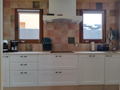 a kitchen with white cabinets and two windows at Casa Lily in Caleta De Fuste
