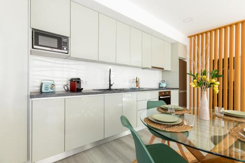 a kitchen with white cabinets and a glass table at Casa na Areia in Leiria