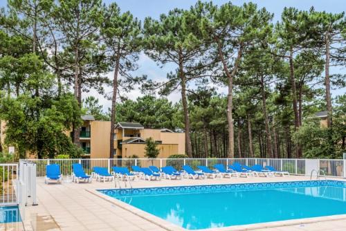 - une piscine avec des chaises longues bleues et des arbres dans l'établissement Résidence Les Grands Pins - maeva Home - Appartement 2 pièces 5 personnes - Prestige MAE-3024, à Maubuisson
