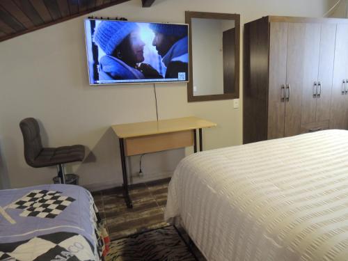 a bedroom with a bed and a desk with a tv on the wall at Pousada Cusco - Centro de Jaraguá do Sul in Jaraguá do Sul