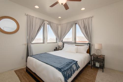 a bedroom with a bed with a ceiling fan and windows at The Sunrise Suite private Hot Tub and shared pool in Joshua Tree