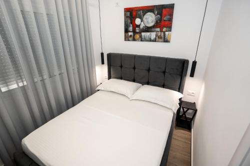 a small bedroom with a white bed with a black headboard at Sunnydream Apartaments Saranda in Sarandë