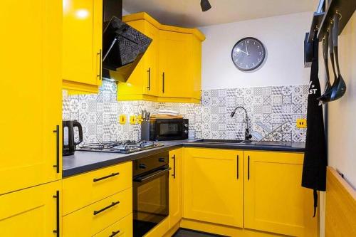 a yellow kitchen with yellow cabinets and a clock on the wall at Funky City Apartment - Secure Parking - WiFi - Sleeps 6 - No Parties in Belfast