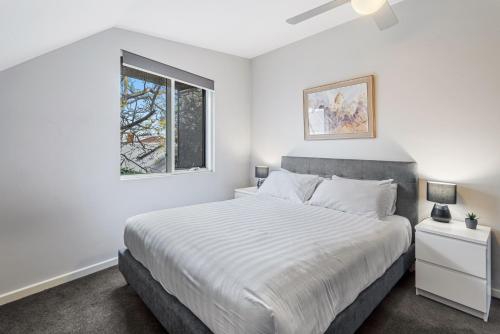 a white bedroom with a bed and a window at Convenient Bayside Living at the Edge of the City in Melbourne