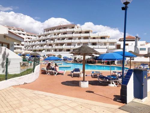 a hotel with a pool with people sitting in chairs and umbrellas at Apartamento Elisa en Garden City con piscina climatizada in Playa Fañabe