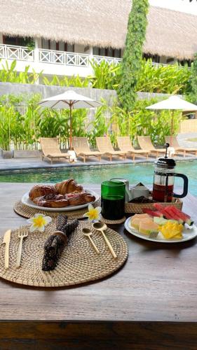 ein Tisch mit Tellern voller Essen neben einem Pool in der Unterkunft Kayu Village in Canggu