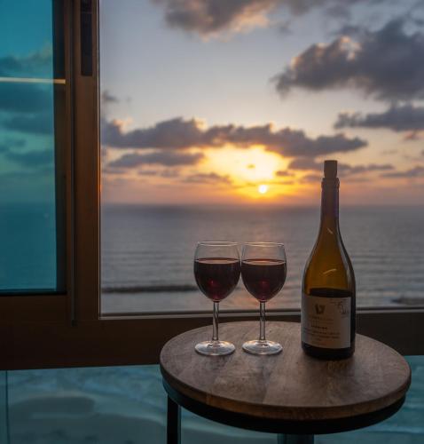 a bottle of wine and two glasses on a table with the sunset at Panoramic Sea View Luxury Suite in Netanya