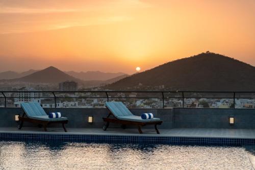 two chairs on the edge of a pool with the sunset at Ramada Encore by Wyndham Udaipur Roopnagar in Udaipur