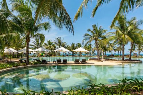 a swimming pool with palm trees and umbrellas at The Pearl Hoi An in Hoi An