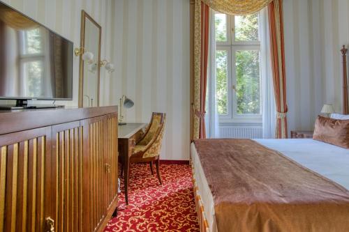 a bedroom with a bed and a desk and a window at Ensana Grand Margaret Island in Budapest