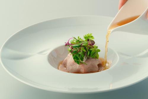 a person is pouring sauce into a bowl of food at Hotel Grand Bach Atami Crescendo in Atami
