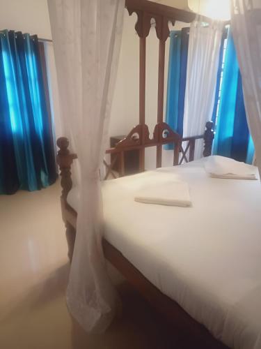 a bedroom with a bed with white sheets and blue curtains at Ronne's Casa De Piscina Privada 3BHK VILLA in Verla