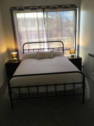 una cama en una habitación con una ventana grande en Luke's Alpine Mountain View rooms, en Jindabyne