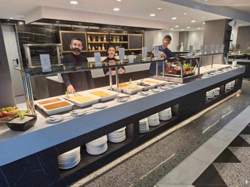 a group of people standing behind a buffet line with food at Kos Palace in Tigaki