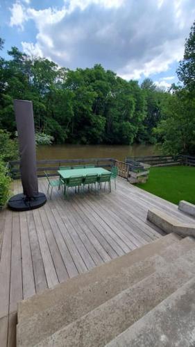 une table de pique-nique verte sur une terrasse en bois avec une rivière dans l'établissement River house with 3 bedrooms, à Montigny-sur-Loing