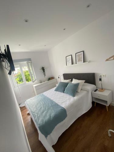 une chambre blanche avec un grand lit avec des oreillers bleus dans l'établissement Apartamento El Baluarte, à Cudillero