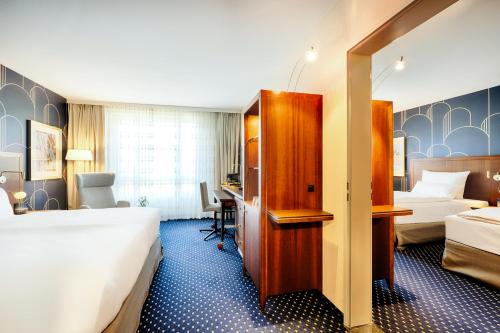 a hotel room with two beds and a desk at Welcome Parkhotel Bochum in Bochum