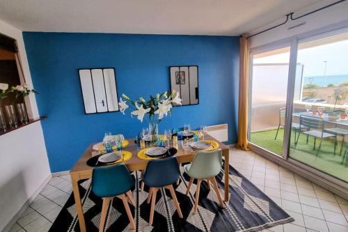 une salle à manger avec une table, des chaises et un mur bleu dans l'établissement LE MARTY 7 Vue Mer Centre Terrasse Garage Piscine Climatisation, à Sète