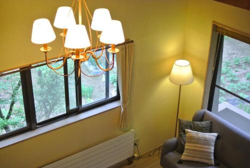 a room with a chandelier and a chair and two windows at 貸切別荘Madoyaのお宿 Loiseau bleu Iizuna in Chūsha