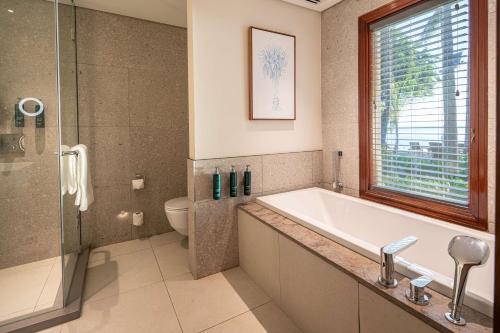 a bathroom with a tub and a toilet and a window at Hilton Mauritius Resort & Spa in Flic-en-Flac