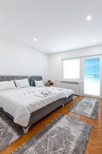 a white bedroom with a large bed and two rugs at Evergreen Apartments in Visoko
