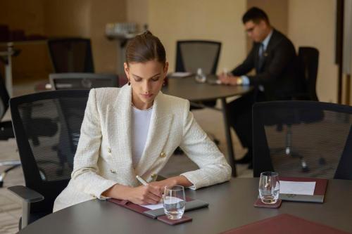 a woman sitting at a table writing on a clipboard at Mansard Riyadh, a Radisson Collection Hotel in Riyadh