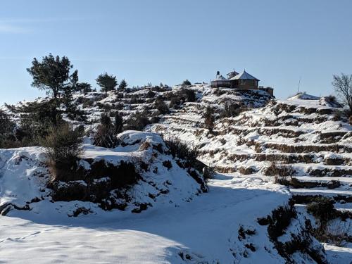 a snow covered hill with a house on top of it at Wild orchid trail cottages in Jhatingr