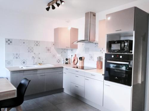 une cuisine avec des armoires blanches et un appareil noir dans l'établissement Au coeur du médoc, La p'tite maison de Charlotte, à Cissac-Médoc