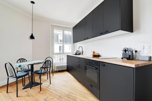 une cuisine avec des armoires noires, une table et des chaises dans l'établissement GuestReady - Parisian elegance in the 19th Arr., à Paris