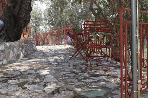 a red fence with a bench next to a tree at Δωμάτια Κόκκινος Πύργος in Plomarion