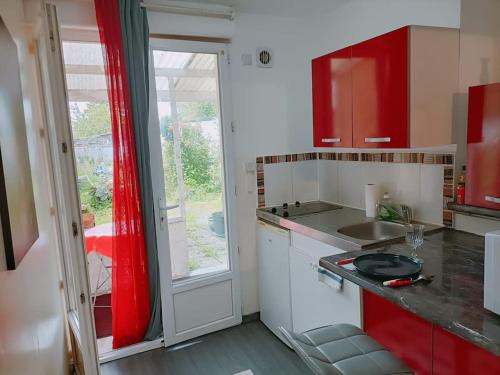 Elle comprend une petite cuisine avec des placards rouges et une fenêtre. dans l'établissement Studio fonctionnel au calme, à Franqueville-Saint-Pierre