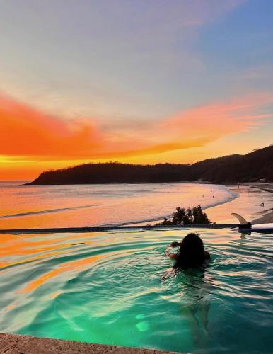 a woman swimming in a pool on a beach at sunset at The Flamingo Experience in San Juan del Sur