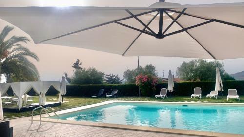 a swimming pool with a white umbrella and chairs at Country Hotel & Resort I Calanchi in Ripatransone