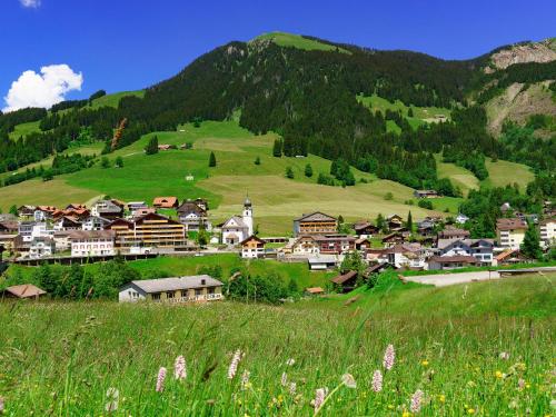 a village in the mountains with a green hill at Heimatli - moderne Ferienwohnung im Sörenberg in Sörenberg
