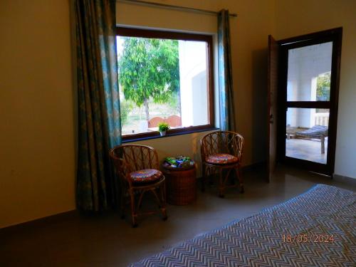a bedroom with two chairs and a large window at Sariska Farms in Tehla