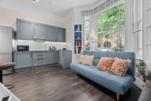 a living room with a blue couch and a kitchen at VICHY - The Hampstead Star | Prime Location in London
