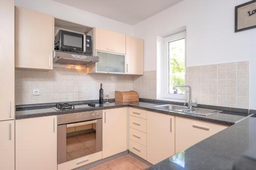 ボルにあるVilla Dalmatia Apartmentsの白いキャビネットとシンクと電子レンジを備えたキッチン