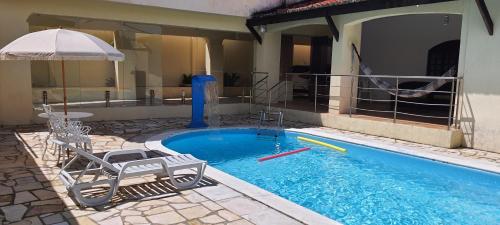 una piscina con dos sillas y una sombrilla en Conforto e Diversão em Ponta Neg, Casa com Piscina, Próxima à Praia e Comodidades Completa, en Natal