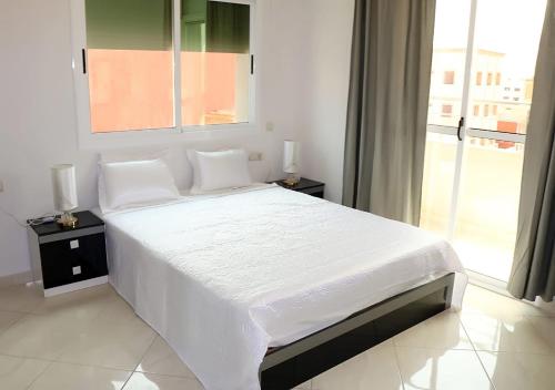 een wit bed in een slaapkamer met een groot raam bij Résidence riad al andalos in Nador