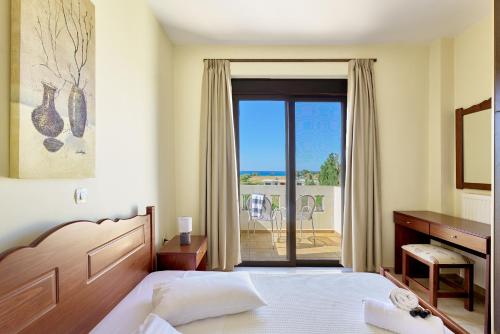 a bedroom with a bed and a desk and a balcony at Villa Gereoudis SeaView Apartments-Pool & Bar in Kolymvari