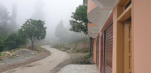 a dirt road with a building and a tree on the side at Mashal Palace Apartment's in Nathia Gali