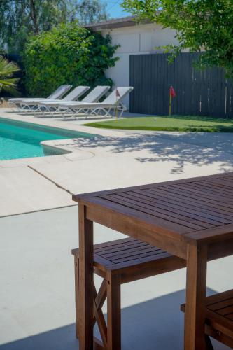 a wooden picnic table next to a swimming pool at The Pink Cactus - Desert Retreat - Luxe Pool, Golf & Game Room in Indio