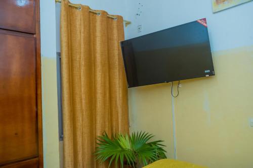 a flat screen tv hanging on a wall with a curtain at AFRIEUROTEXT Kamerun-High Standing-Appartements-Wifi-Security-Restaurant-modern Kitchen in Yaoundé