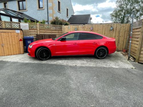 a red car parked in a driveway next to a fence at Pemberton cottage in Ingleton 